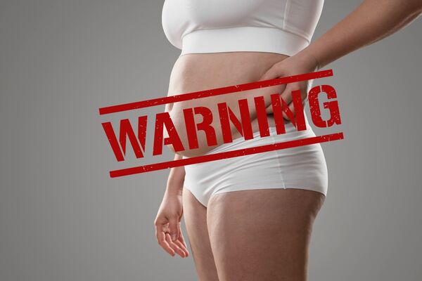 une femme tient ses poignées d'amour sur cette photo un warning en rouge